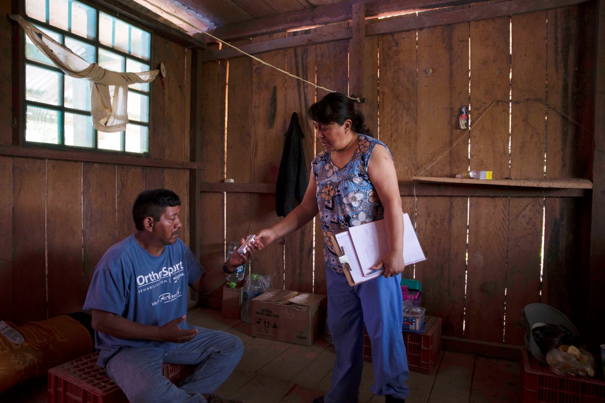 Gimena Gutierrez, a doctor, has health responsibilities in the Yuqui community. Here she gives medicine to former village leader Jhonathan Isategua. Image by Sara Aliaga. Bolivia, 2020. Gimena Gutierrez, a doctor, has health responsibilities in the Yuqui community. Here she gives medicine to former village leader Jhonathan Isategua. Image by Sara Aliaga. Bolivia, 2020.