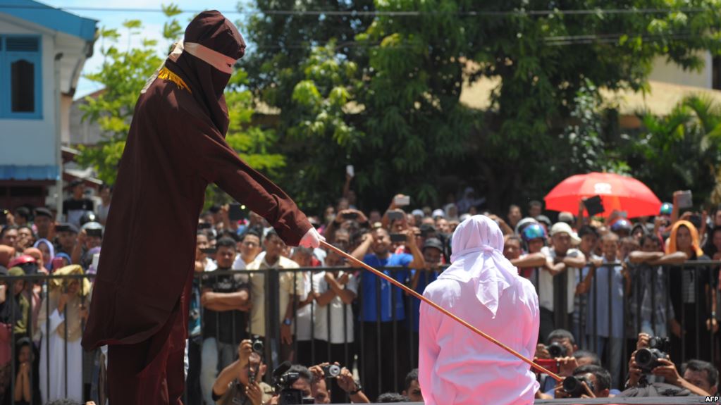 A religious officer canes an Acehnese youth onstage as punishment for dating outside marriage, which is against Sharia, or Islamic law, outside a mosque in Banda Aceh, Aug. 1, 2016. Aceh's landscape is dotted with Saudi influence, but its religious climate is decidedly not. Image from AFP. Indonesia, 2016. A religious officer canes an Acehnese youth onstage as punishment for dating outside marriage, which is against Sharia, or Islamic law, outside a mosque in Banda Aceh, Aug. 1, 2016. Aceh's landscape is dotted with Saudi influence, but its religious climate is decidedly not. Image from AFP. Indonesia, 2016.
