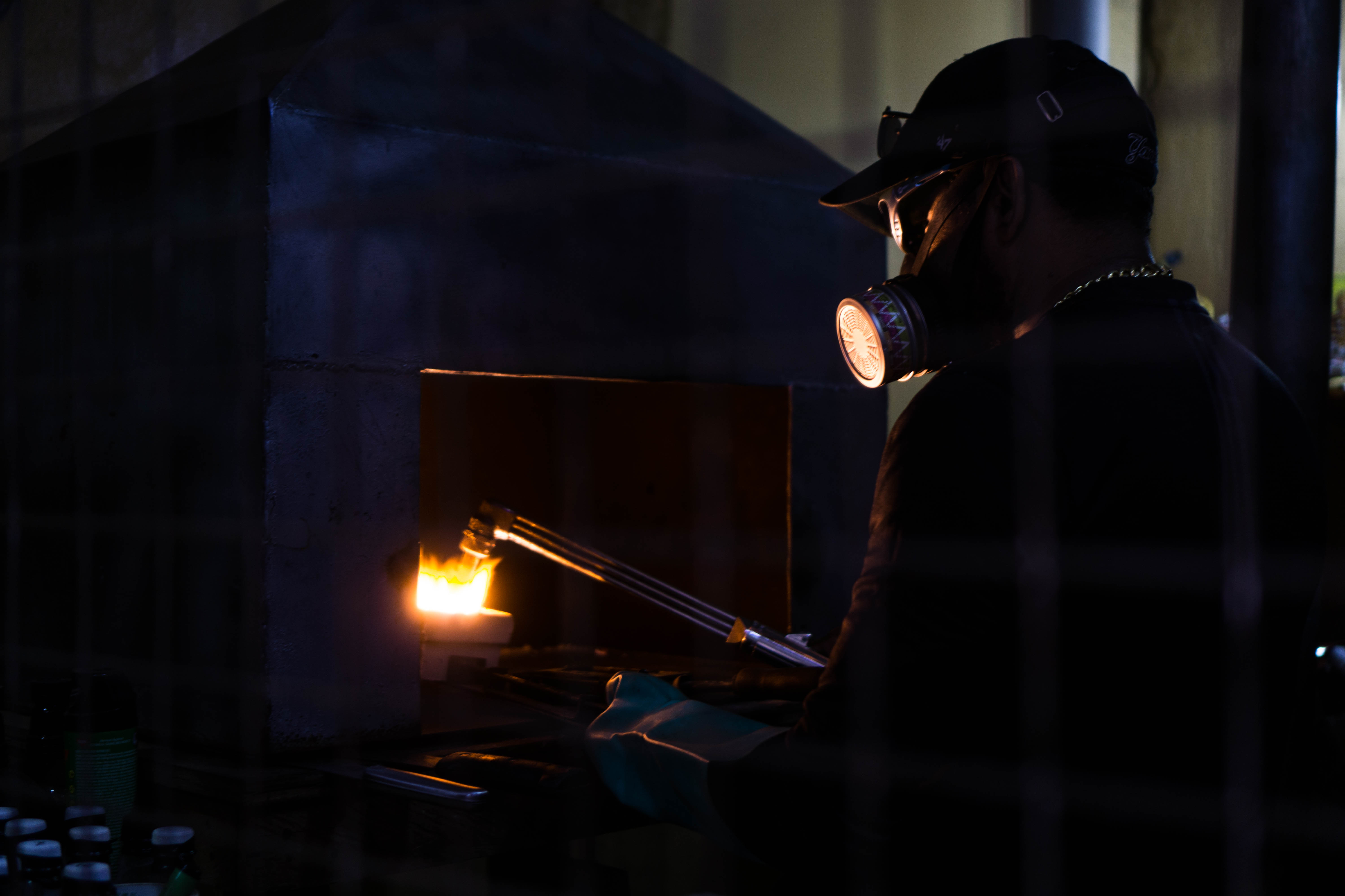 Man in a small refinery melts gold and burns the mercury. He uses a mask to avoid the toxic vapor