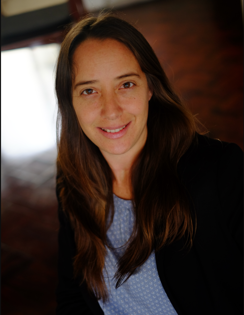 A woman wears a black jacket and blue blouse.