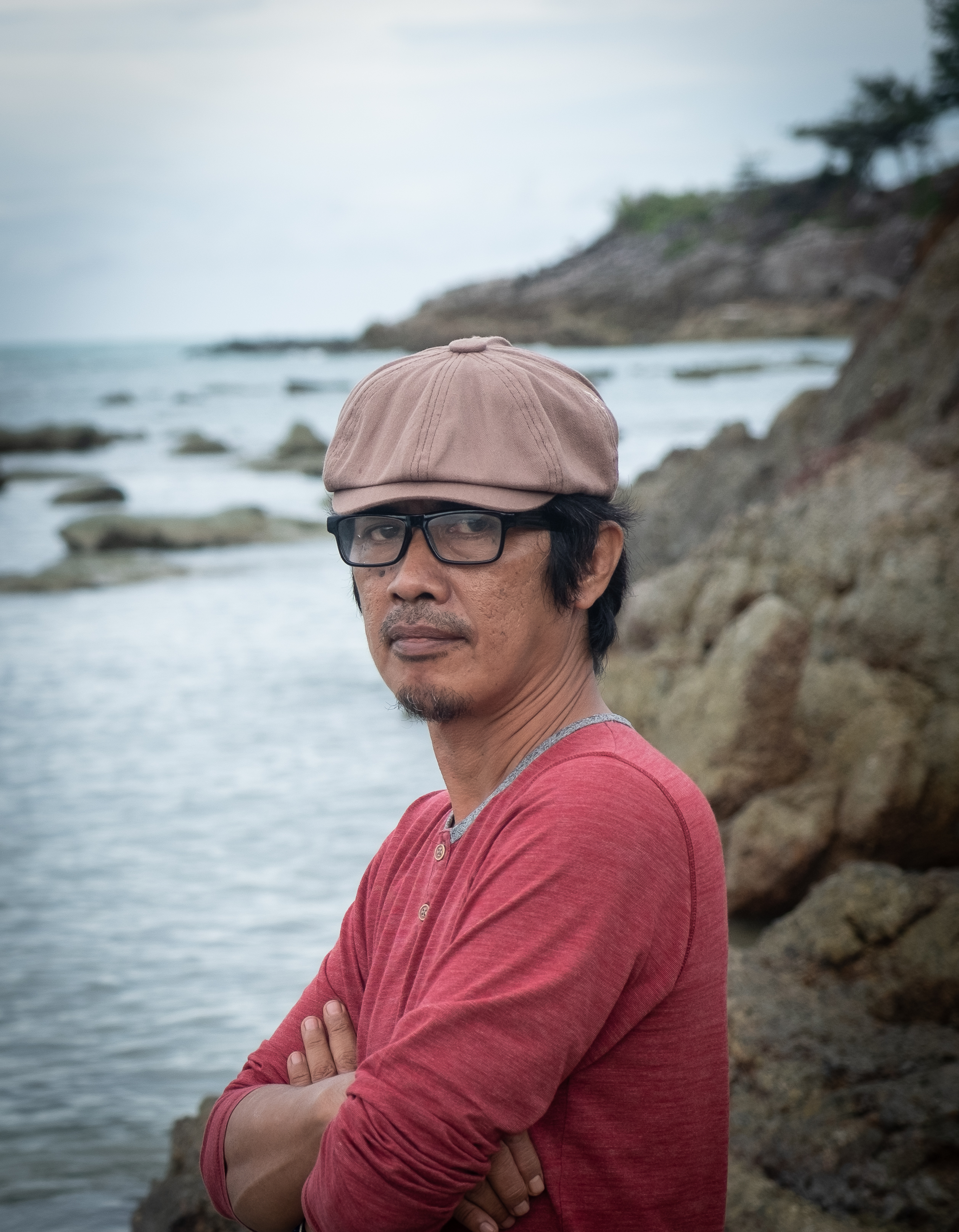 A person wears glasses, a brown baseball cap, and a red shirt.