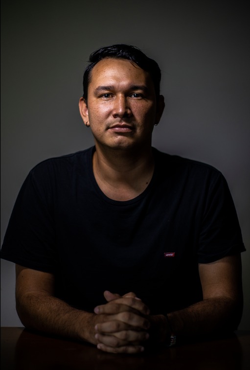 A man with dark hair looks into the camera