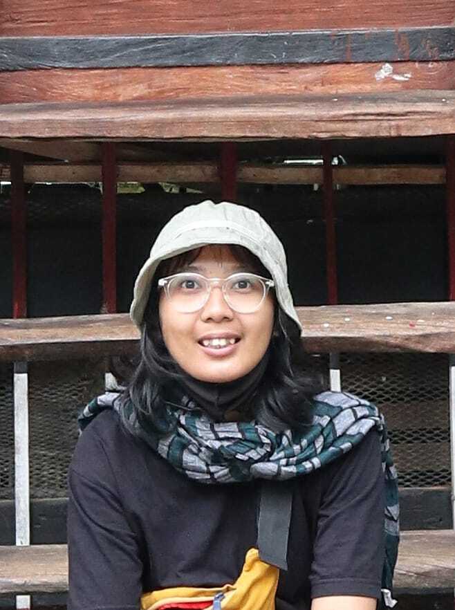 A person wears a cap and glasses. She is also wearing a black long sleeve shirt.