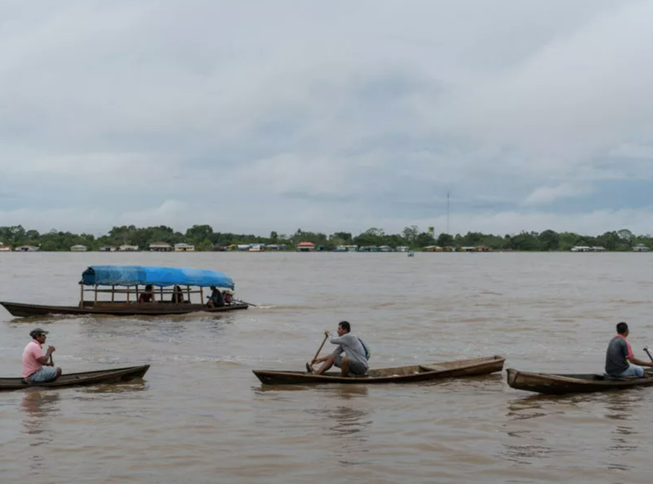 Canoes row across quiet, turbid waters.