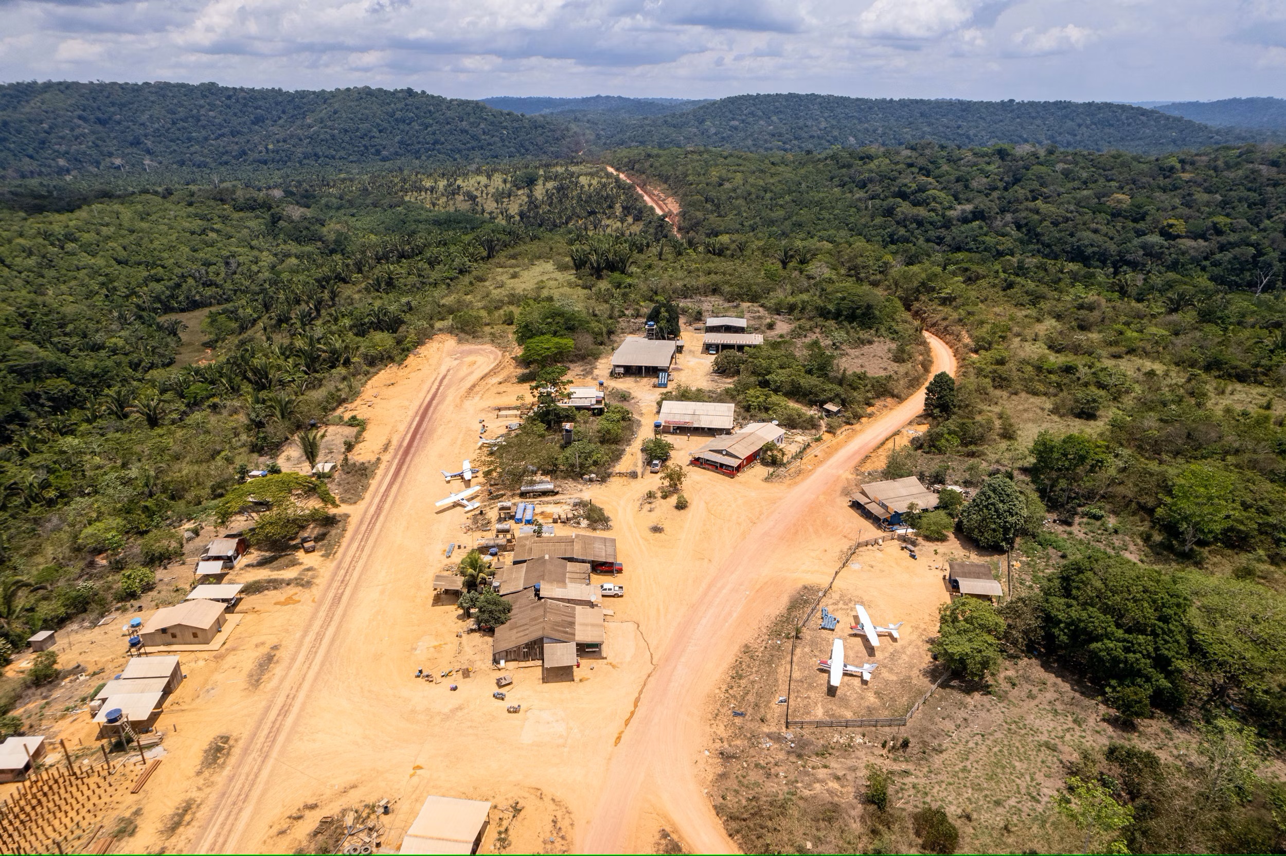 aerial view of a small settlement set around a dirt airstrip in the middle of thick vegetation
