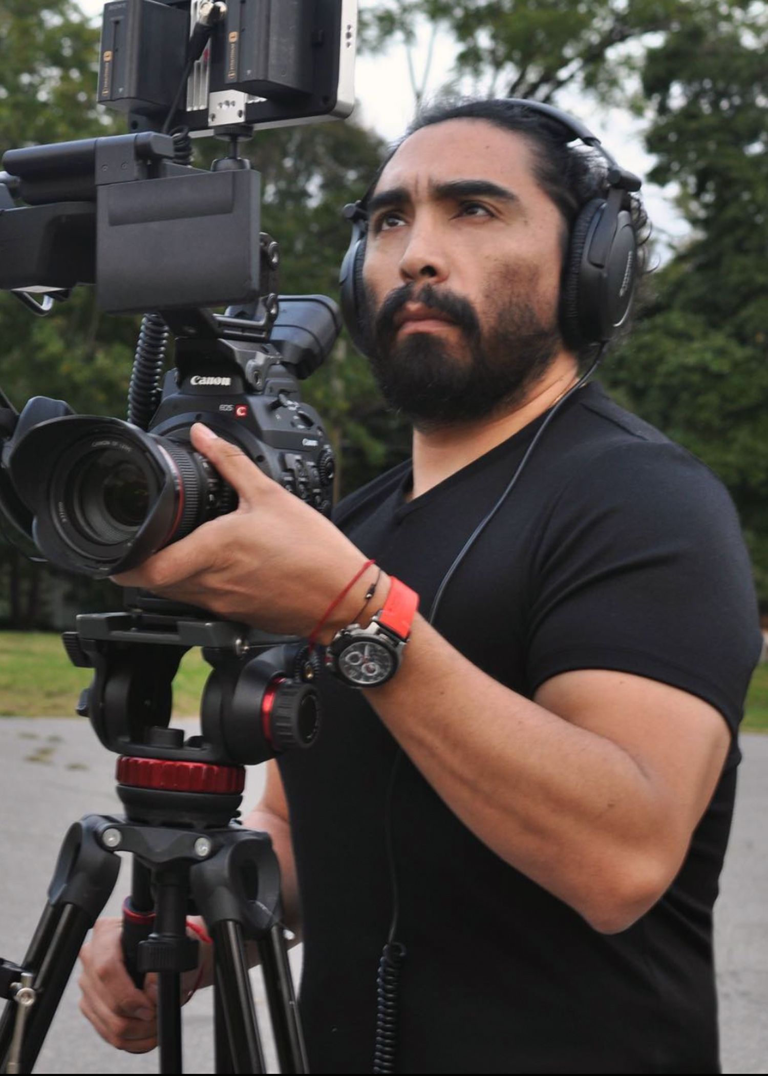 Enrique Huaiquil holds a camera that is set up on a tripod. He wears headphones and focuses on the camera.