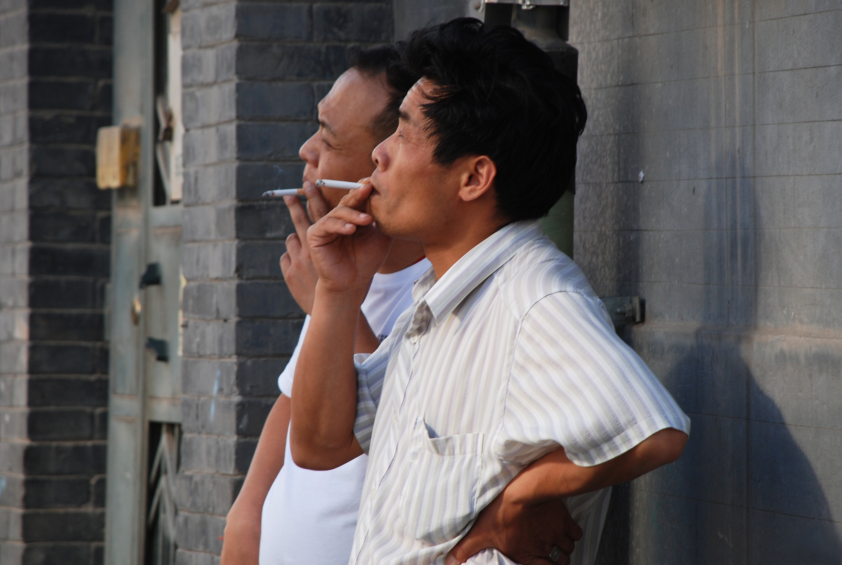 two men lean against a wall for a smoke break