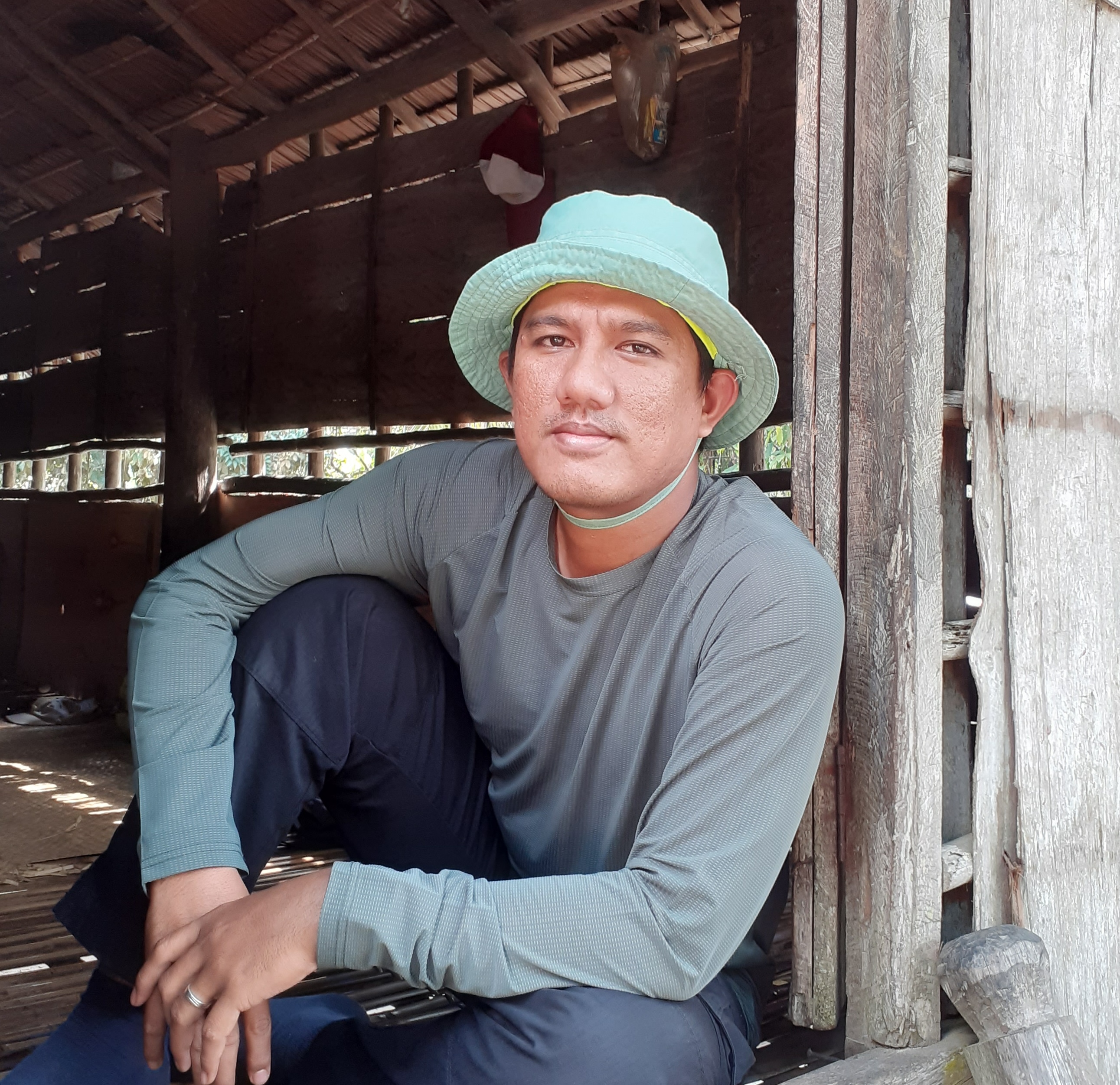 Suryadi sits on a threshold wearing a bucket hat.