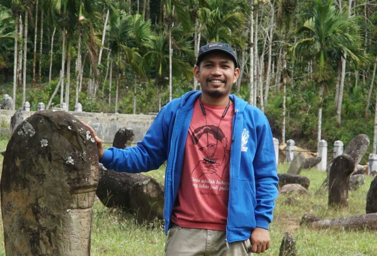 A man is smiling wearing a red shirt and blue jacket.
