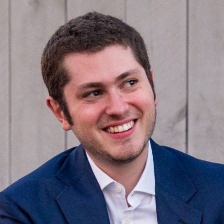 A man with short hair wearing a white button down and blue blazer