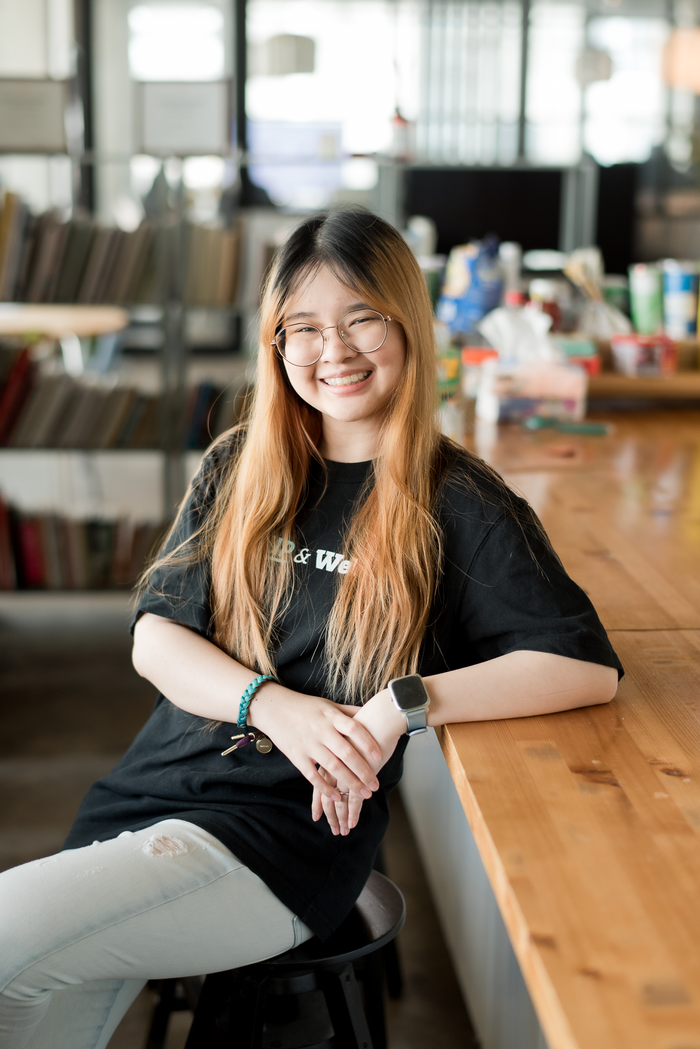 Pitshaya wearing a black tee leans back on a table and smiles into the camera.
