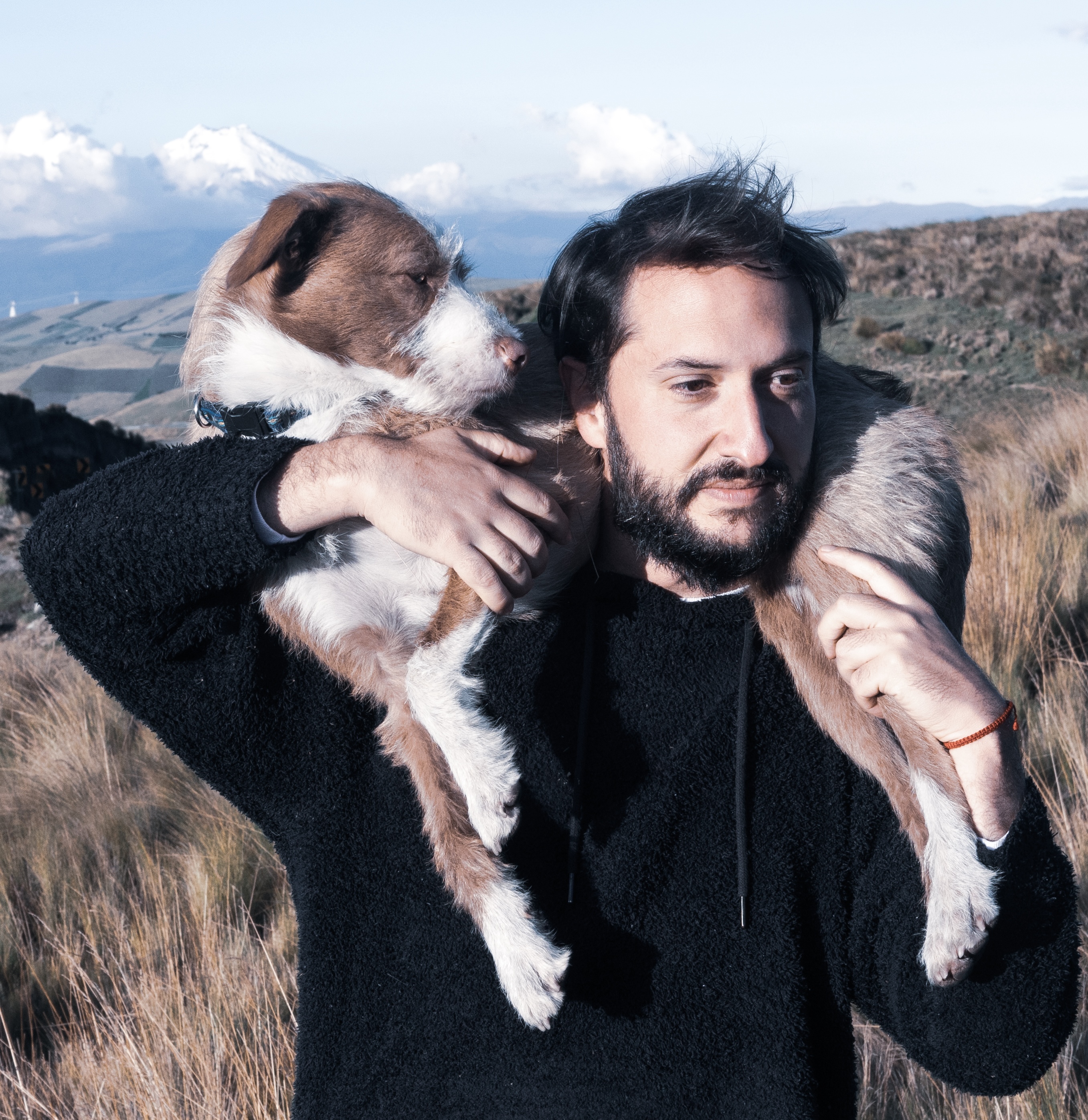 Mijail aA dog is wrapped around Mijail's shoulders against beautiful mountains.