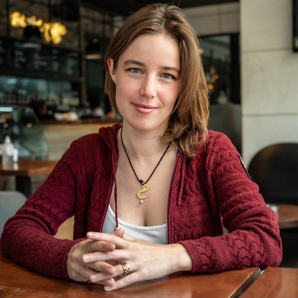 Aisha sits at a table wearing a red cardigan