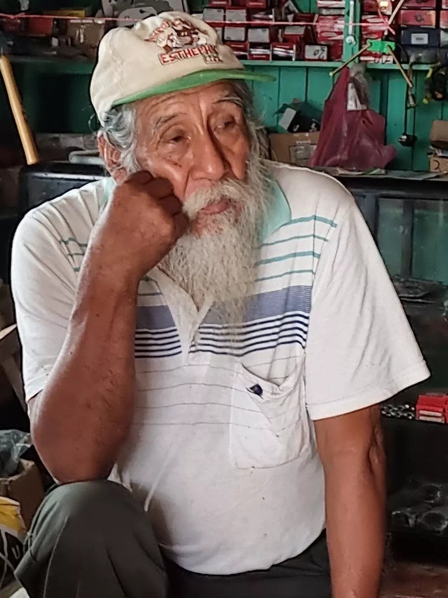 Albino Ramos sits with his elbow on his knee wearing an old cap and a long white beard. 