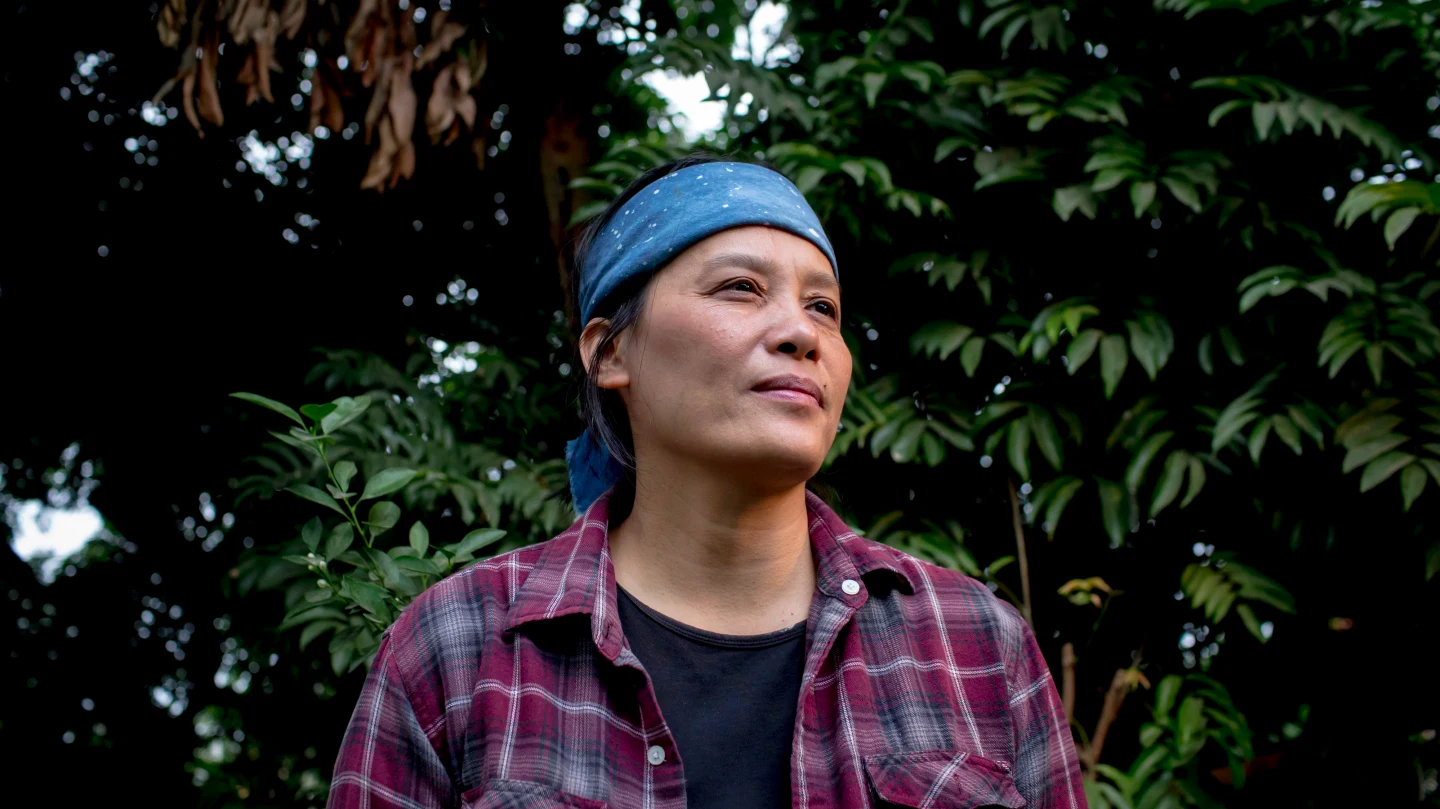 a vietnamese woman wearing a black t shirt, red flannel, and blue bandana around her forehead, standing in the forest