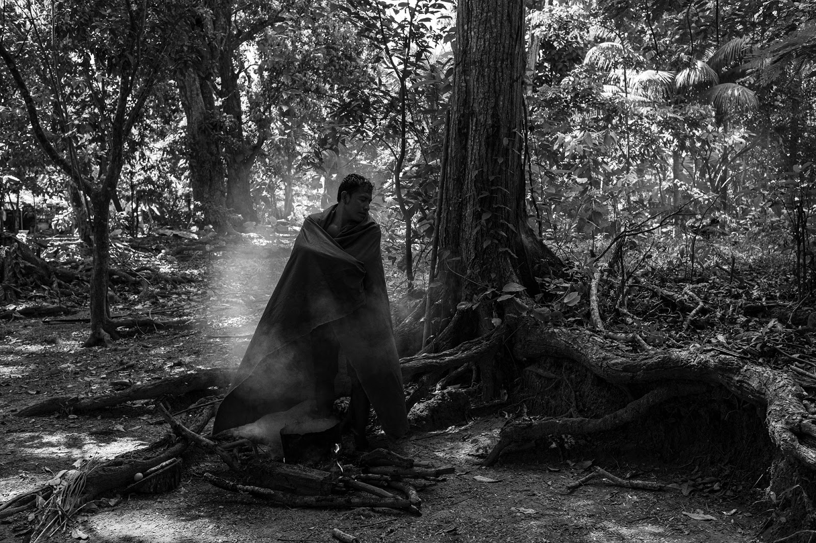 A man wearing a cape and standing in the middle of vapors in the forest.