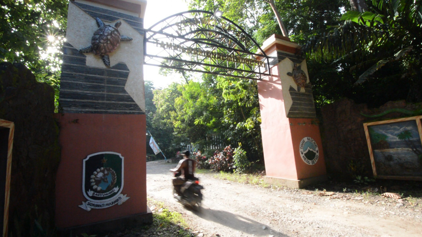 A person on a motorcycle drives through the entrance gate to Meru Betiri National Park.
