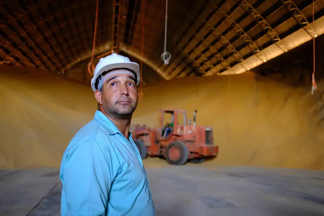 A worker at Grupo Vale do Verde looks on as grain is moved at one of its many facilities in the state of Mato Grosso. Big Ag in Brazil wants to see better transport options, including the construction of a railway, the Ferrogrão — “the grain train” — that would cut across the jungle. Image by Melissa Chan. Brazil, 2019. A worker at Grupo Vale do Verde looks on as grain is moved at one of its many facilities in the state of Mato Grosso. Big Ag in Brazil wants to see better transport options, including the construction of a railway, the Ferrogrão — “the grain train” — that would cut across the jungle. Image by Melissa Chan. Brazil, 2019.