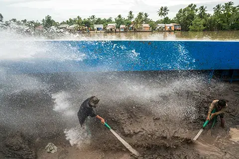 Sand barge workers near Can Tho City hose down a mountain of sand pumped up from branches of the Mekong. The wet sand is then pumped through underground pipes to a road construction site further inland.