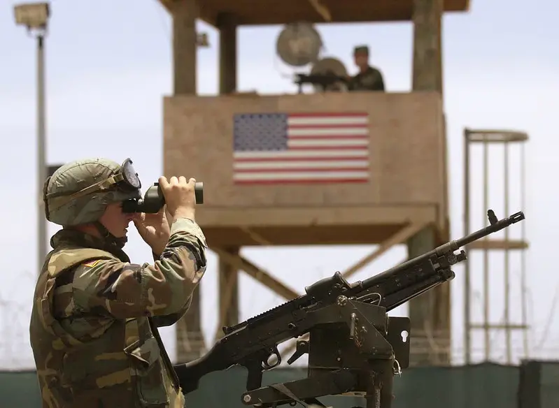 A soldier atop a High Mobility Multipurpose Wheeled Vehicle (HMMWV) surveys the area just outside Camp Delta during a detainee escape exercise in Guantanamo Bay, Cuba. Image by U.S. Navy photo by Journalist Chief (SS) John F. Williams. Cuba, 2003.