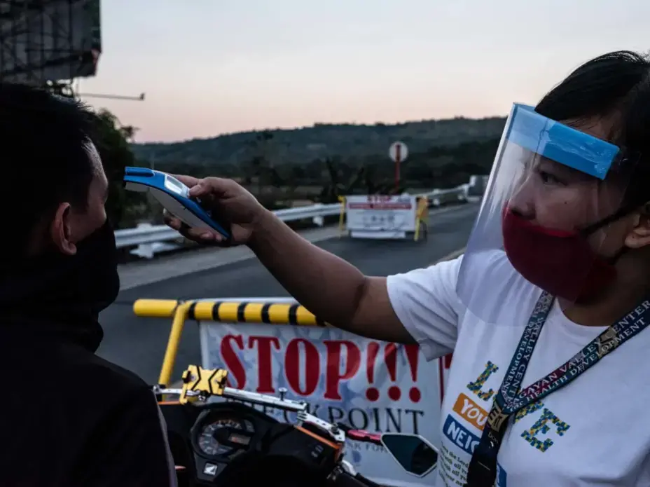 Rose Ann, a rural nurse, checks the temperature of a traveler at a checkpoint. Image by Xyza Bacani. Philippines, 2020.