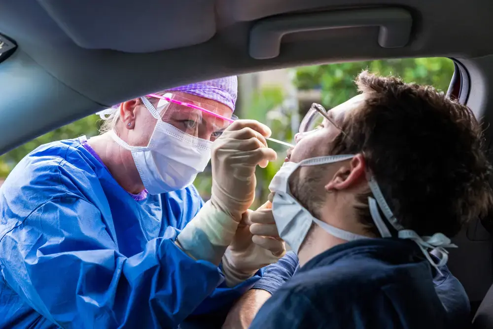 A doctor in a protective suit taking a nasal swab from a person to test for possible coronavirus infection. Image by zstock / Shutterstock. United States, 2020.