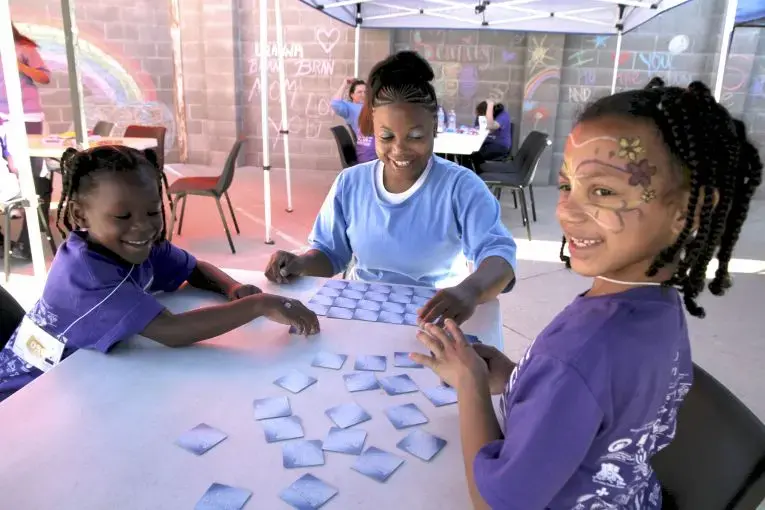 Mi'Angel (left) and Mayal enjoy a card game with their mom, Donisha. From 2018 article, "Visiting Day". Image by Jaime Joyce. United States, 2018.