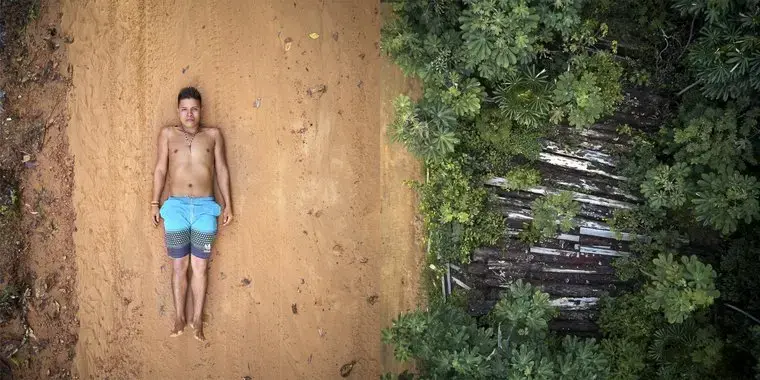 Ednei poses on the tracks left by the trucks used to transport wood that pass through the borders of his territory. Right: what's left of 26 trees destroyed by illegal lumberjacks in indigenous Maró territory. Image by Pablo Albarenga. Brazil, 2019. Ednei poses on the tracks left by the trucks used to transport wood that pass through the borders of his territory. Right: what's left of 26 trees destroyed by illegal lumberjacks in indigenous Maró territory. Image by Pablo Albarenga. Brazil, 2019.