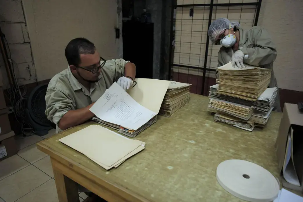 Archivist Oscar Hernández, left, cleans and sorts a file of documents concerning police detention of children and minors in the 1980s. Hernández, 34, was a young boy when his father was abducted by the National Police. In the course of his daily work at the archive, he has discovered some clues to his father’s disappearance, but he may never know the full story. Image by Lynn Johnson. Guatemala, 2017.
