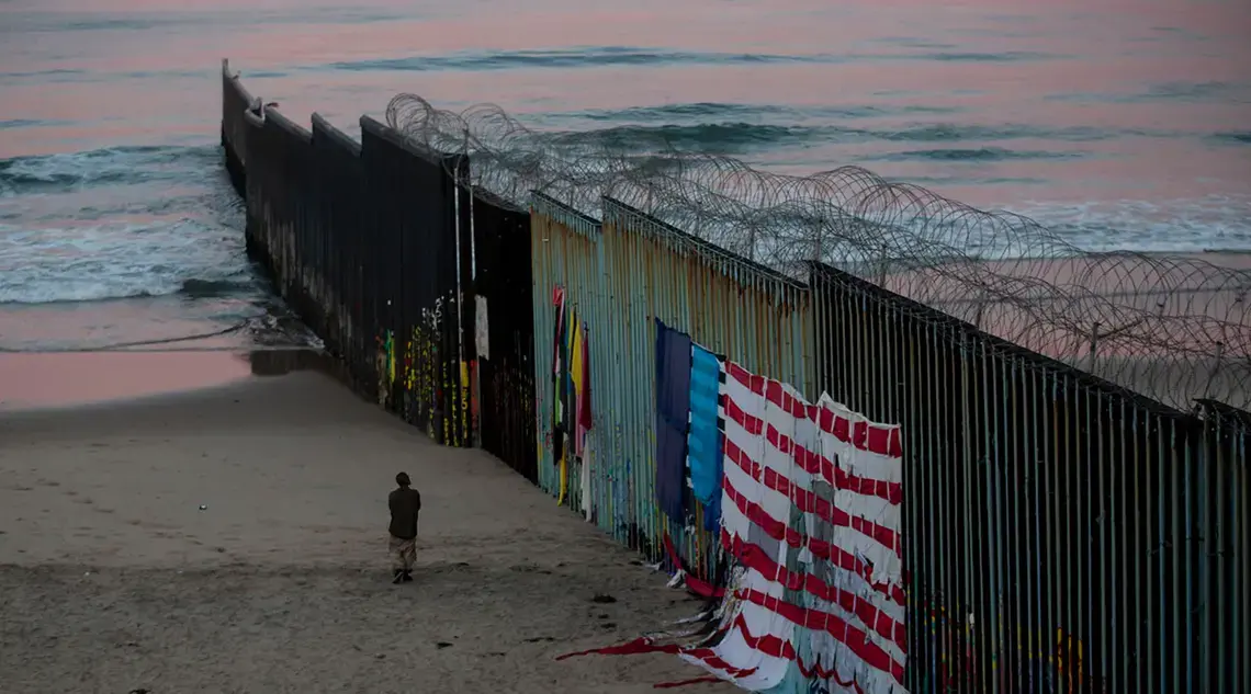 In Tijuana, a man walks at sunrise along the border fence where it meets the Pacific Ocean. Image by Erika Schultz. Mexico, 2019.