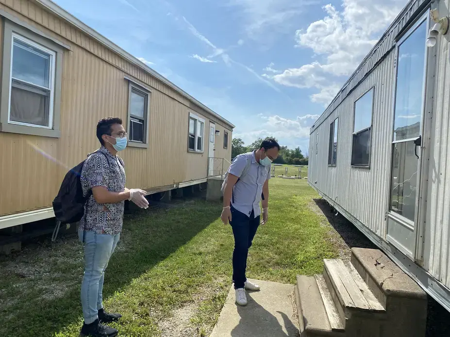 FLOC members Lorenzo Zamora (left) and Braulio Franco (right) wait outside for a farmworker to answer the door during their visit to Liskai Farms migrant camp. Image by Areeba Shah. United States, 2020.