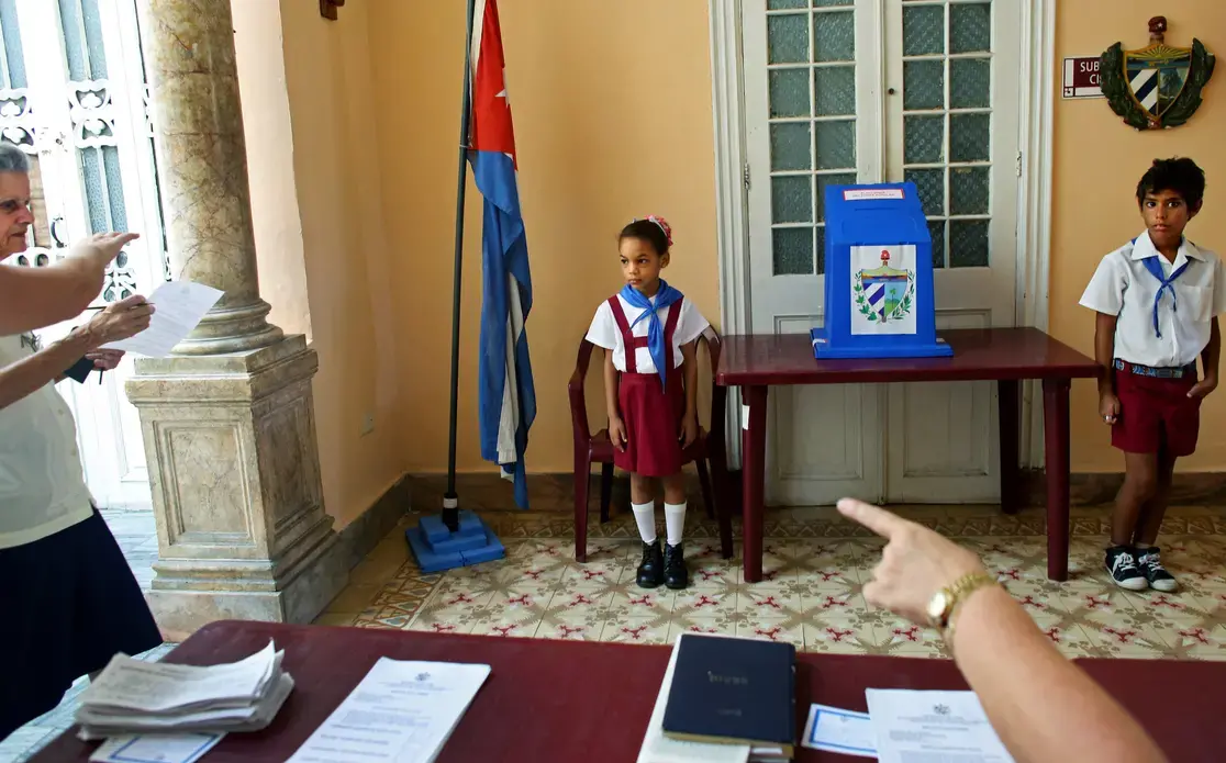 Children wearing the uniform of Communist youth are prepared to salute “Votó!” (“He voted!”), as a woman places her ballot in Cuba’s Elecciones Parciales (Partial Elections). The vote was to elect delegates to the Municipal Assemblies of People’s Power, the country’s unicameral parliament, on April 19, in Havana. The delegates function as district representatives for a two-and-a-half-year term. Image by Yana Paskova. Cuba, 2015.