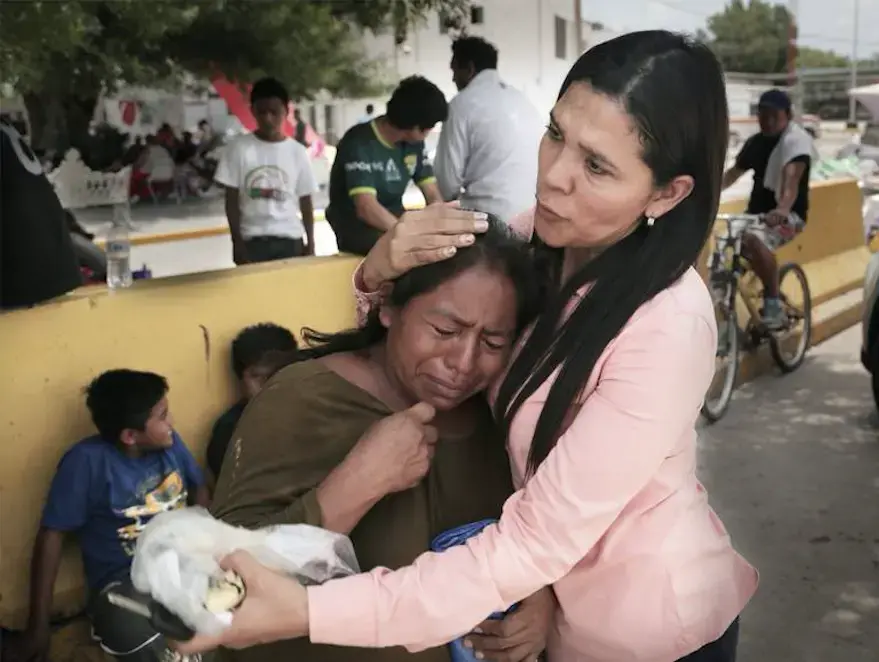 Gladys Edil Caas, a local Mexican volunteer who delivers water, blankets and other needs to migrants camped out by the bridge, consoles a Guatemalan woman during a visit to the camp. Image by Jose A Iglesias. Mexico, 2019.