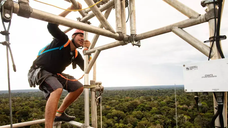 Researcher Delano Campos scales an 80-meter tower at the Amazon Tall Tower Observatory to collect air samples and maintain instruments. Image by Victor Moriyama. Brazil, 2019. Researcher Delano Campos scales an 80-meter tower at the Amazon Tall Tower Observatory to collect air samples and maintain instruments. Image by Victor Moriyama. Brazil, 2019.