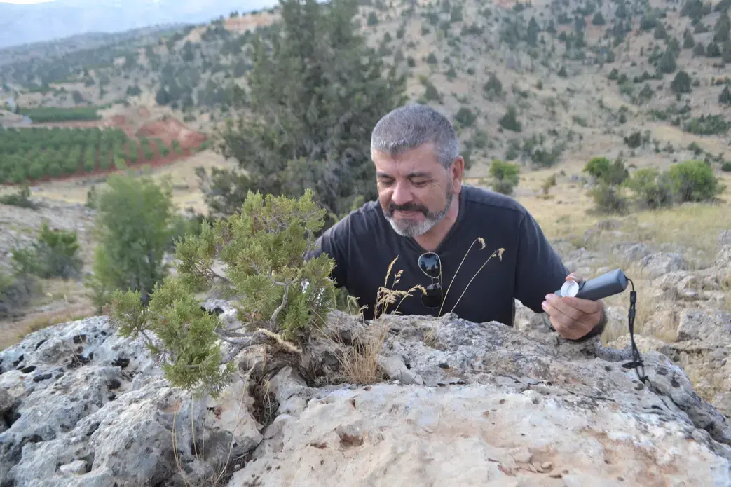 Antoine Geagea greets and waters a juniper tree growing on top of a boulder. Image by Catherine Cartier. Lebanon, 2019.