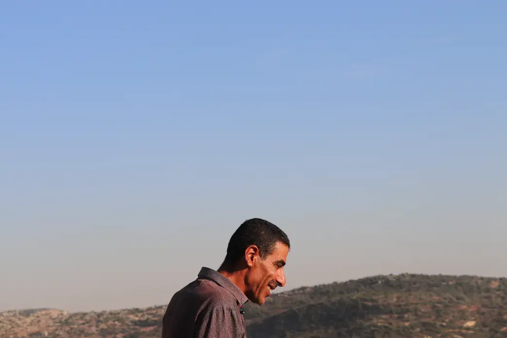 A farmer in Burqin, an agricultural village in the West Bank, stands on what's left of his olive groves. In January 2019, he received an order from the Israeli Civil Administration to uproot half his trees. A few weeks later, the remainder were razed. Image by Carly Graf. West Bank, 2019.