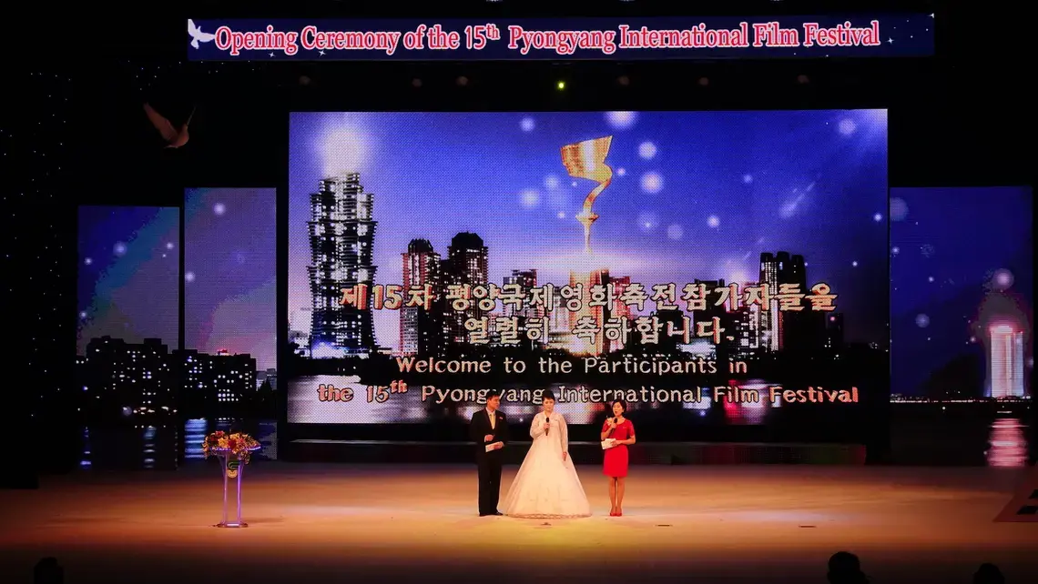 The three hosts on stage during the opening ceremony of the 15th Pyongyang International Film Festival. A sculpted dove in the top left signifies the festival's mission of peace. Image by Laya Maheshwari. North Korea, 2016.