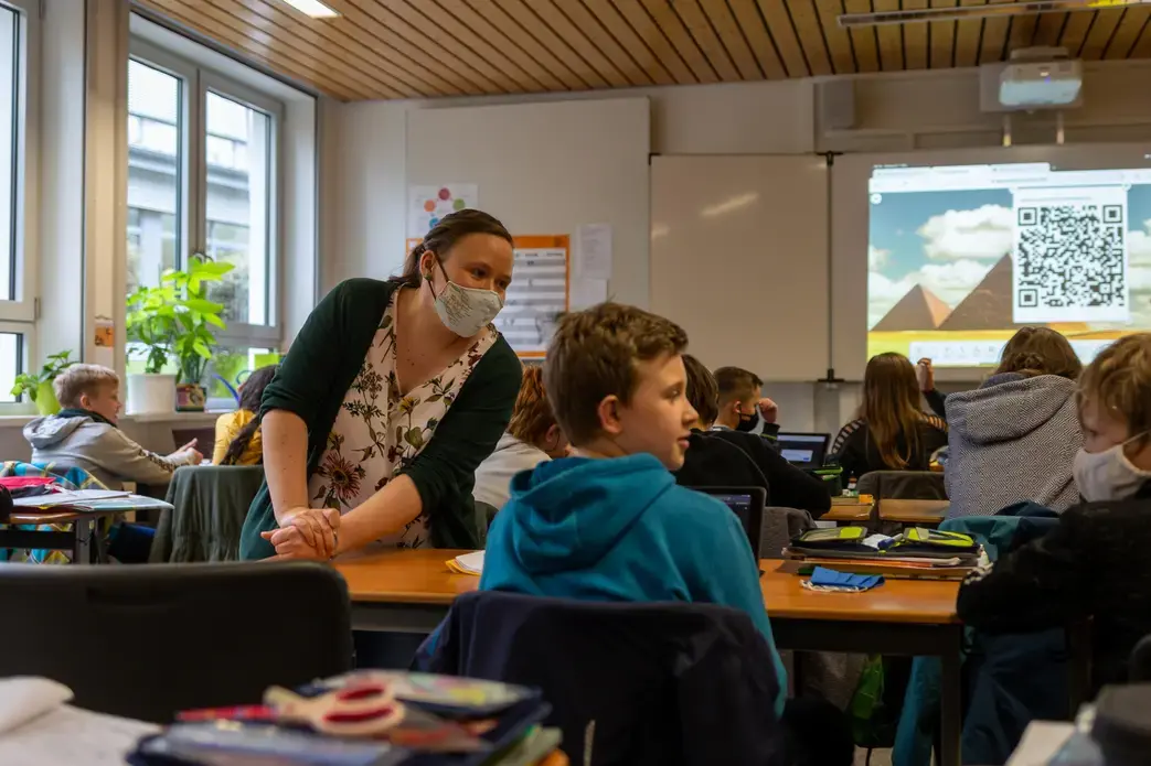 Teacher Inga Deppa works with students in an English class at Jacobishule in Kalletal, Germany. Masks were optional for students when they were seated at their desks, but the regional health authority has since tightened mask rules for older students. Image by Ryan Delaney. Germany, 2020.
