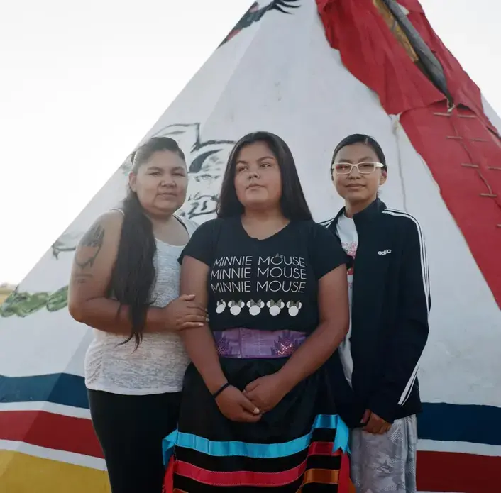 Prairiedawn Thunderchild (right), 16, with her sister Tahnee Thunderchild (center), 14, and their mother. The sisters were almost abducted a year ago by a vehicle of oil workers in Wolf Point. Image by Sara Hylton. United States, 2019.