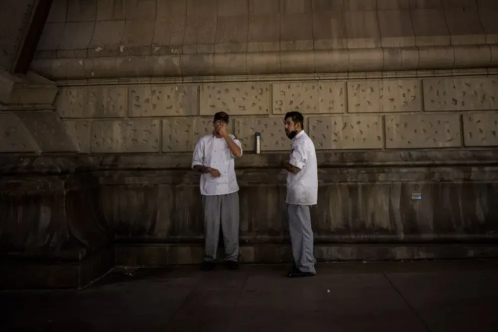 Workers take a cigarette break outside the Bellagio in Las Vegas, Monday, Nov. 9, 2020. To be an immigrant in Las Vegas is to see the coronavirus economy at its worst. Visitors to the area plummeted by more than 90 percent in a little over a month. The state's unemployment rocketed to 28 percent, the worst in the nation and a level not seen even during the Great Depression.&nbsp;Image by Wong Maye-E / AP Photo. United States, 2020.