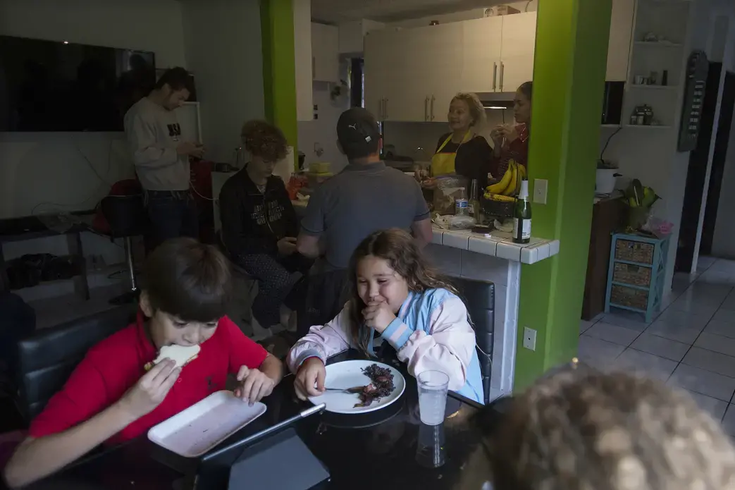 Edward Flores enjoys a white bread sandwich made with Nutella while his siter, Rayma, enjoys a plate of their mother's Cuban black beans and rice at lunchtime Nov. 29 in their father's apartment in Tijuana, Mexico. The times when the entire family can all be together are rare. Image by Amanda Cowan. Mexico, 2019.