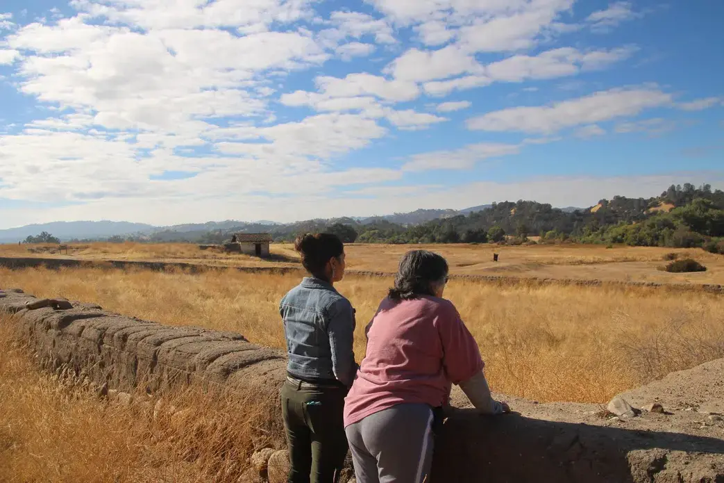 Allison Herrera and Mary Bishop, both Salinan Indians, look out at the Indian Cemetery at the San Antonio Mission in Lockwood, California. 
The cemetery was laid out in 1804 at the height of the mission building period in California. Missions were built by California Indians through force. The total number of California Indians laid out in this cemetery is unknown, although Mary said it was in the thousands. Image by Isaac Kestenbaum. California, 2017.