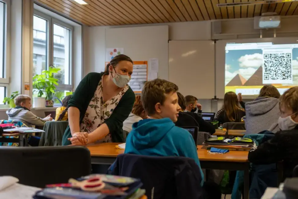 Teacher Inga Deppa works with students in an English class at Jacobishule in Kalletal, Germany. Masks were optional for students when they were seated at their desks, but the regional health authority has since tightened mask rules for older students. Image by Ryan Delaney/St. Louis Public Radio. Germany, 2020.