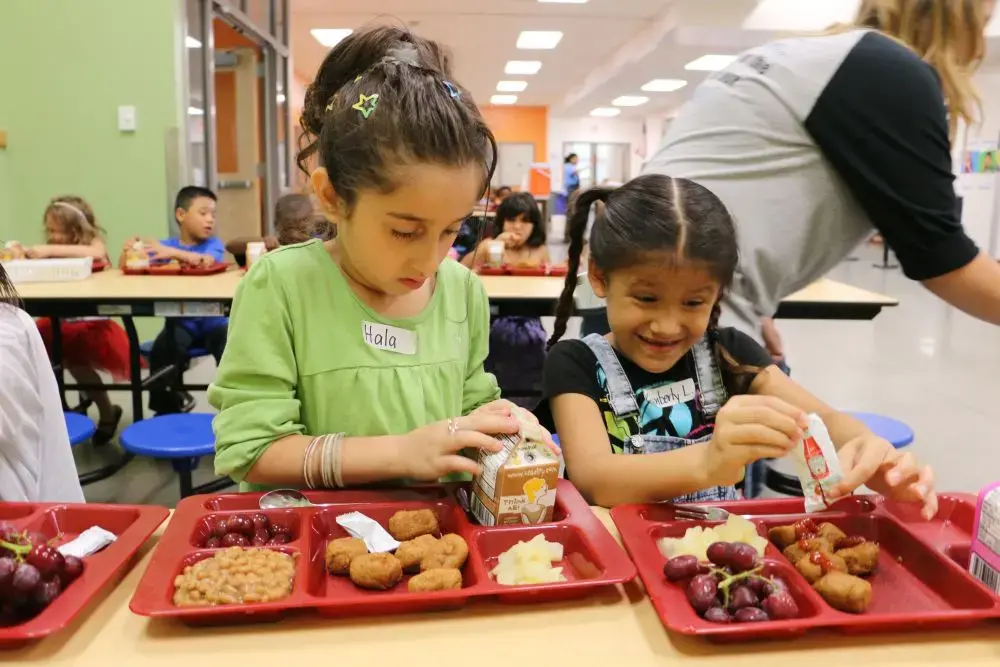 The food at school is unfamiliar. Hala just pokes at her "wiener dogs." She struggles to open a milk carton while the girl beside her wrestles with a ketchup packet