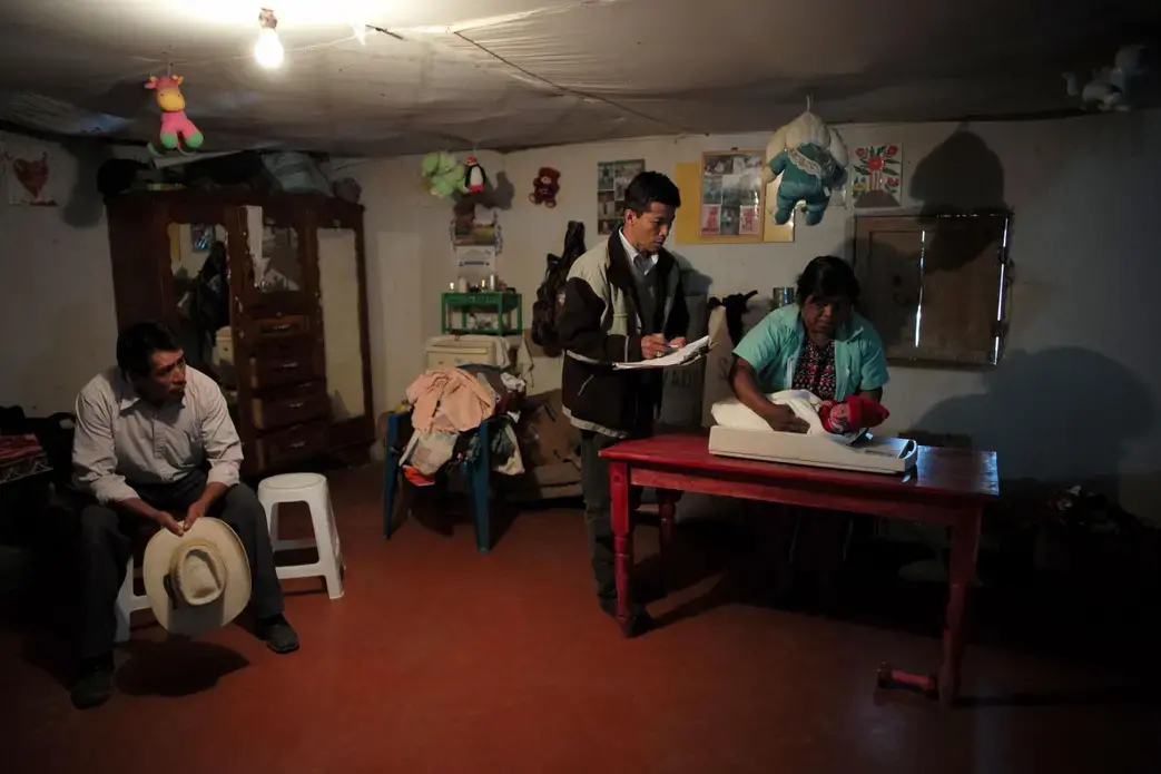 Midwife Expedita Ramírez Marroquín, a member of the research team, weighs and examines a baby born that day, as a health worker and the baby’s grandfather (with cowboy hat) look on. Cleaner indoor in Guatemala is not just a matter of more money and better stoves; there are cultural barriers. Right after this photo was taken, the baby’s mother entered a chuj—a traditional Mam sauna heated by a smoky wood fire—for a ritual postpartum cleansing. Image by Lynn Johnson. Guatemala, 2017.