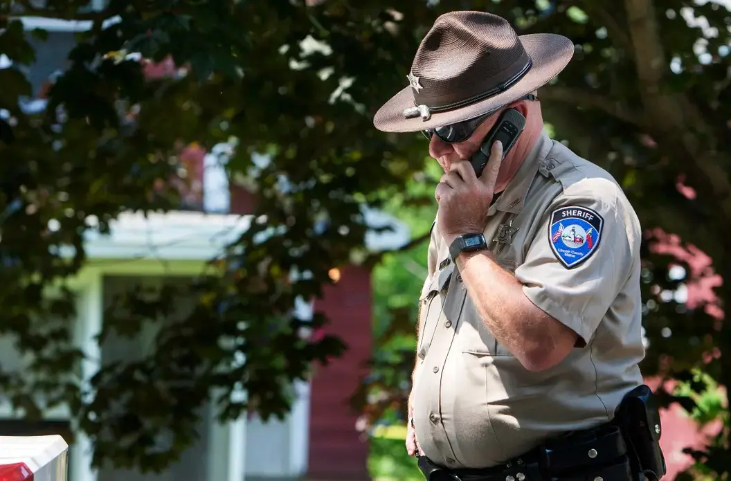 A deputy with the Lincoln County Sheriff's Office takes a phone call outside the scene of an investigation in Boothbay Harbor in this 2015 file photo. Image by Ashley L. Conti/BDN. United States, 2015.