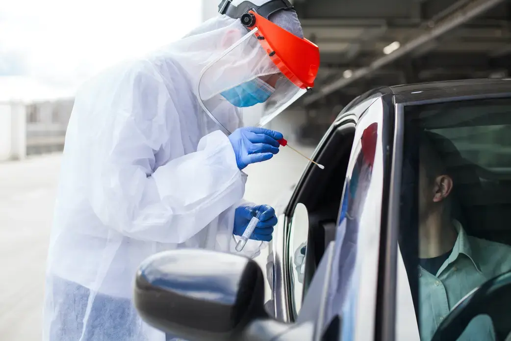 A medical worker administers a COVID-19 swab at a mobile testing center. In the fall of 2020, Novavax launched a phase III COVID-19 vaccine trial in the United Kingdom. Image by Cryptographer / Shutterstock. United Kingdom, 2020.