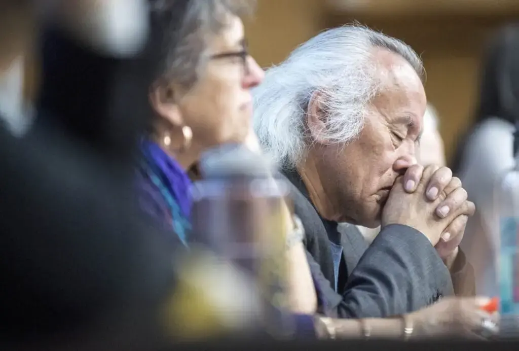 Tommy Monias from the Pimicikamak Territory in Manitoba, Canada, holds his head in his hands as a friend speaks about the impacts on their land from 'mega-dam' hydropower in Manitoba during a speaking tour at Preble Hall at the University of Maine in Farmington on Nov. 25, 2019. Image by Michael G. Seamans. United States, 2019.