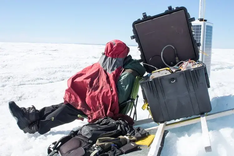 The 24-hour sunlight is so bright that researcher Toby Meierbachtol had to make a tent over his head in order to see the screen of a computer they're using to log the data from the ice sheet bed. Image by Amy Martin. Greenland, 2018. 