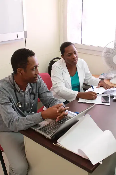 Dr. Joseph Bernard, left, trains another Haitian physician on how to care for cancer patients. Image by Kate Corrigan. Haiti, 2017. 